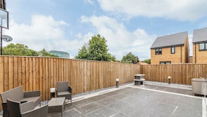 An outdoor patio with wicker furniture, a stone floor, and a wooden fence. - A Stylish, essential 3bed Home with Secure Parking (Nottingham)