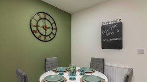 A dining area with a round table set for four, a wall clock, and a motivational sign. - A Stylish, essential 3bed Home with Secure Parking (Nottingham)