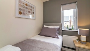 A bedroom with a bed, a bedside table with a lamp, a window with a view, and a framed artwork on the wall. - A Stylish, essential 3bed Home with Secure Parking (Nottingham)