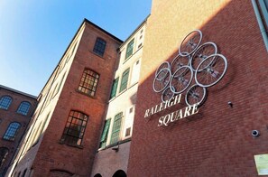 Un bâtiment en briques sur lequel on peut lire l’inscription « RALEIGH SQUARE », et une installation artistique représentant une roue de vélo.