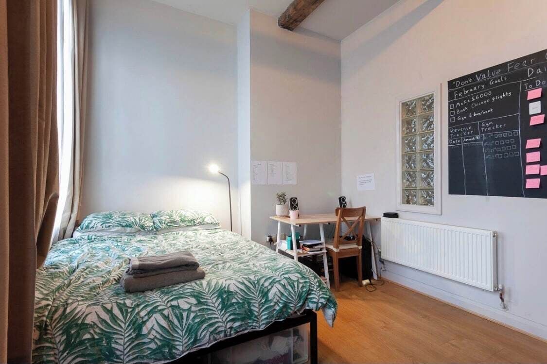 Ein Schlafzimmer mit einem Bett, einem Schreibtisch, einem Stuhl, einem Heizkörper und einer Tafel mit Notizen.