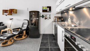 Una cocina moderna con electrodomésticos de acero inoxidable, horno integrado y cafetera. Hay una silla negra y un armario de madera con espacio para vinos.