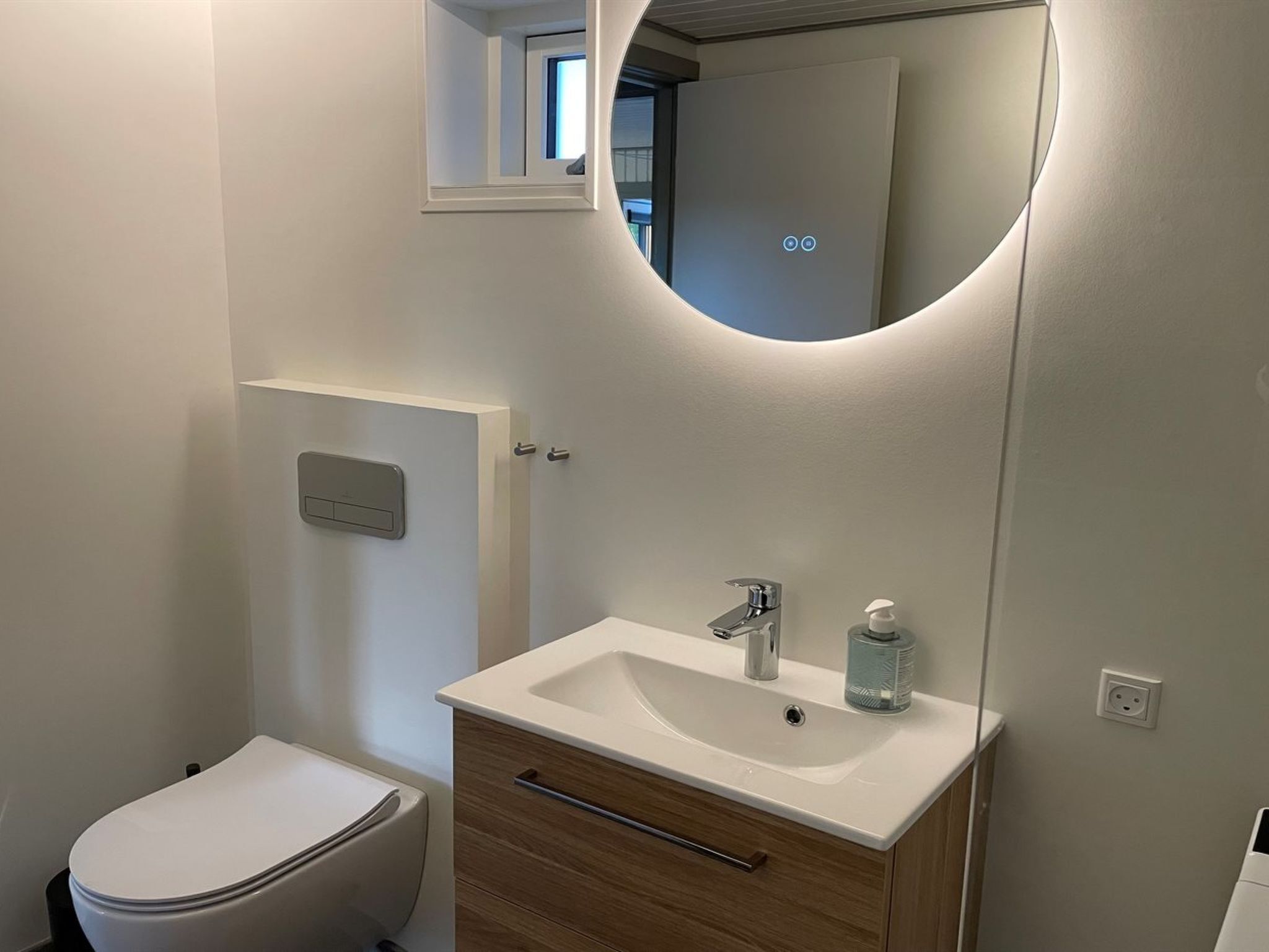 A modern bathroom with a toilet, a sink with a mirror above, and a wooden cabinet below.