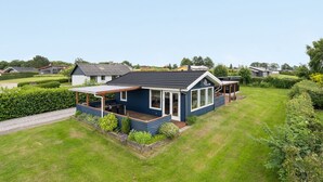 Une maison de plain-pied à l’extérieur d’un bleu foncé, dotée d’un porche et d’une pelouse bien entretenue.