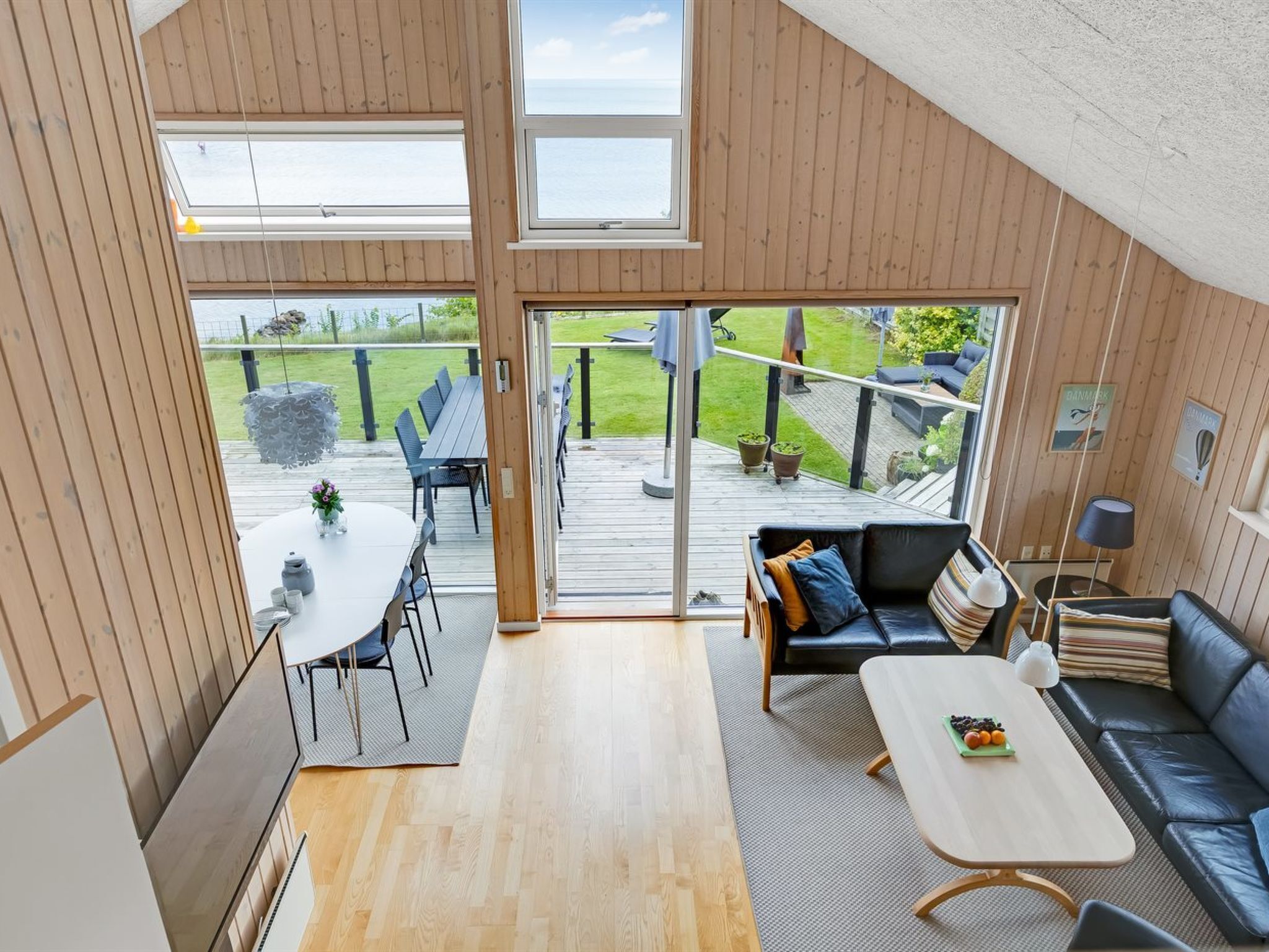 Un intérieur moderne avec une terrasse en bois, un coin repas et un espace de vie comprenant un canapé et une table basse.