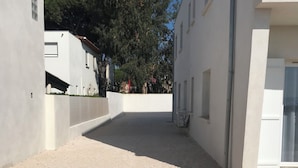 A narrow, gravel-covered alleyway between buildings with white walls and a clear blue sky. - Villa sur la Mer, Refaite à Neuve en Juillet 2023 (Hyères)