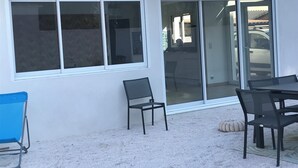 A patio area with a table and chairs, a blue chair, and a large sliding glass door leading to a parking area. - Villa sur la Mer, Refaite à Neuve en Juillet 2023 (Hyères)