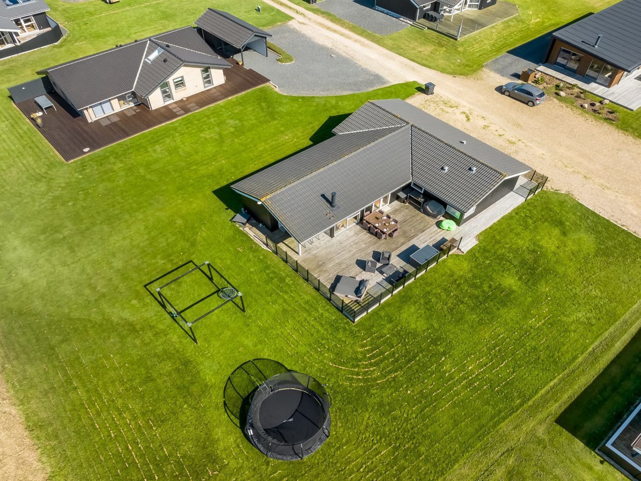 Vue aérienne d’une propriété résidentielle dotée d’une grande terrasse, d’un trampoline et d’un espace salon extérieur abrité.