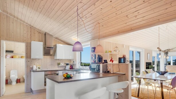 Une cuisine moderne agrémentée d’éléments en bois, un îlot central avec des tabourets de bar et un coin repas offrant une vue agréable.