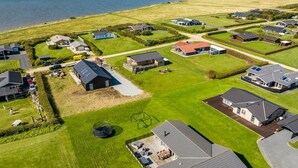Vue aérienne d’un quartier résidentiel situé sur la côte, avec des maisons, une aire de jeux et une vue dégagée sur la mer.