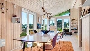 Un espace repas moderne avec une grande table, des chaises colorées et un plafond en bois.