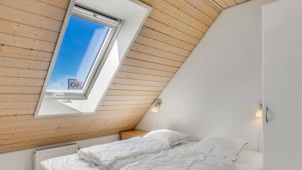 A bedroom with a sloped ceiling, a skylight, a bed with white bedding, a radiator, and a white wardrobe.