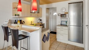 A modern kitchen with a stainless steel refrigerator, wooden ceiling, and pendant lights.