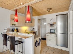 A modern kitchen with a stainless steel refrigerator, wooden ceiling, and pendant lights.