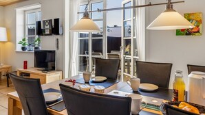A dining area with a table set for four, two pendant lights, a television, and a painting on the wall.