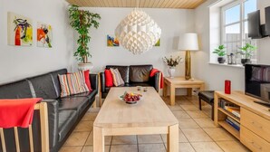 A modern living room with a wooden ceiling, a black leather sofa, a wooden coffee table, and a TV on a wooden stand.