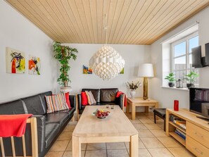 A modern living room with a wooden ceiling, a black leather sofa, a wooden coffee table, and a TV on a wooden stand.