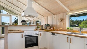 Une cuisine moderne avec des meubles en bois, un four encastré, un lave-vaisselle et une grande fenêtre donnant sur l’extérieur.
