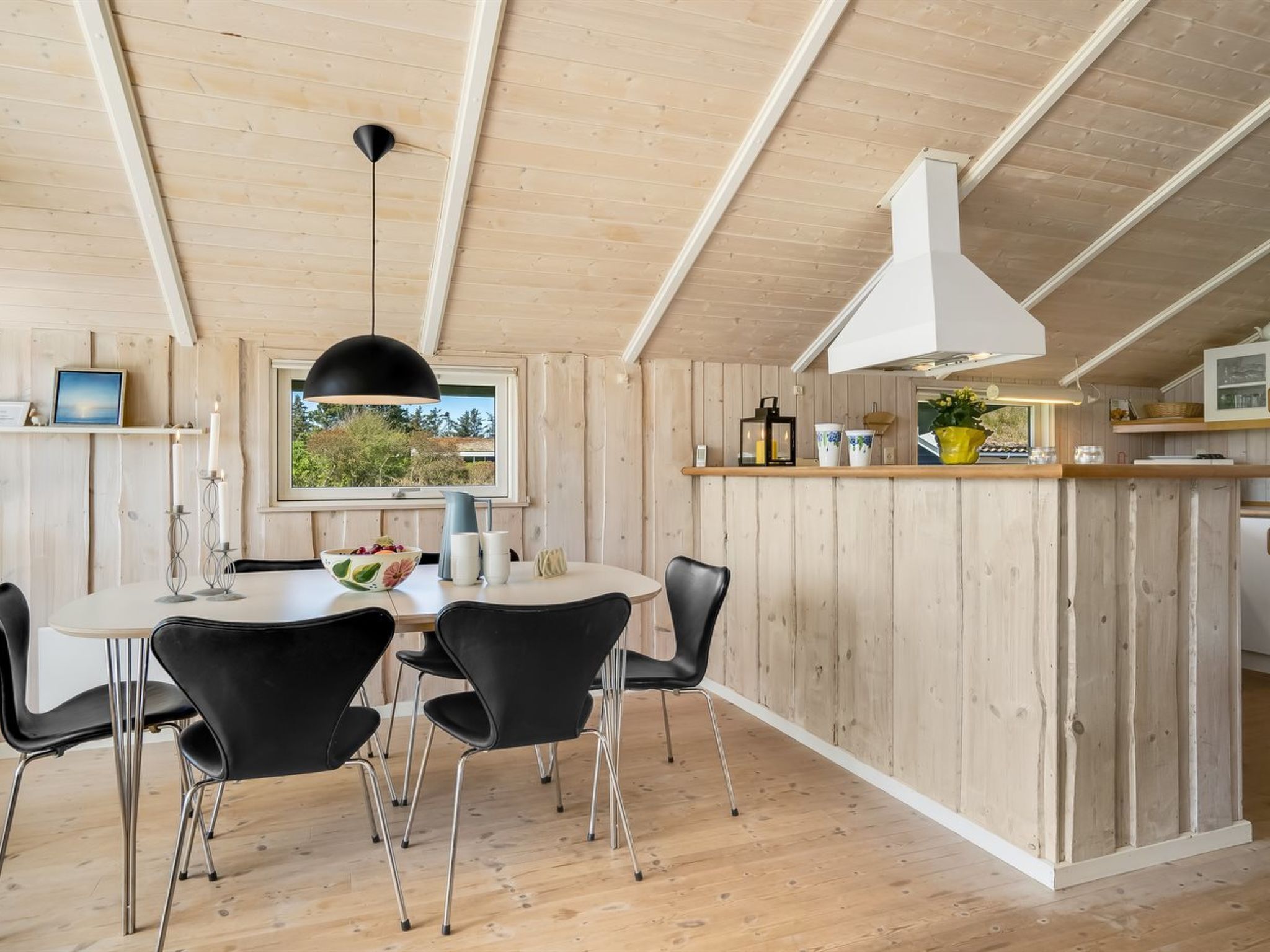 Una cucina moderna con isola centrale, pareti in legno e zona pranzo con sedie nere e tavolo rotondo.