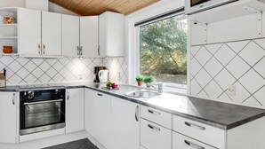 Una cocina moderna con armarios blancos, horno empotrado, microondas y un amplio ventanal con vistas a árboles.