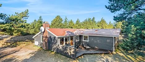 Una casa de un piso con techo inclinado, chimenea y una zona de terraza.