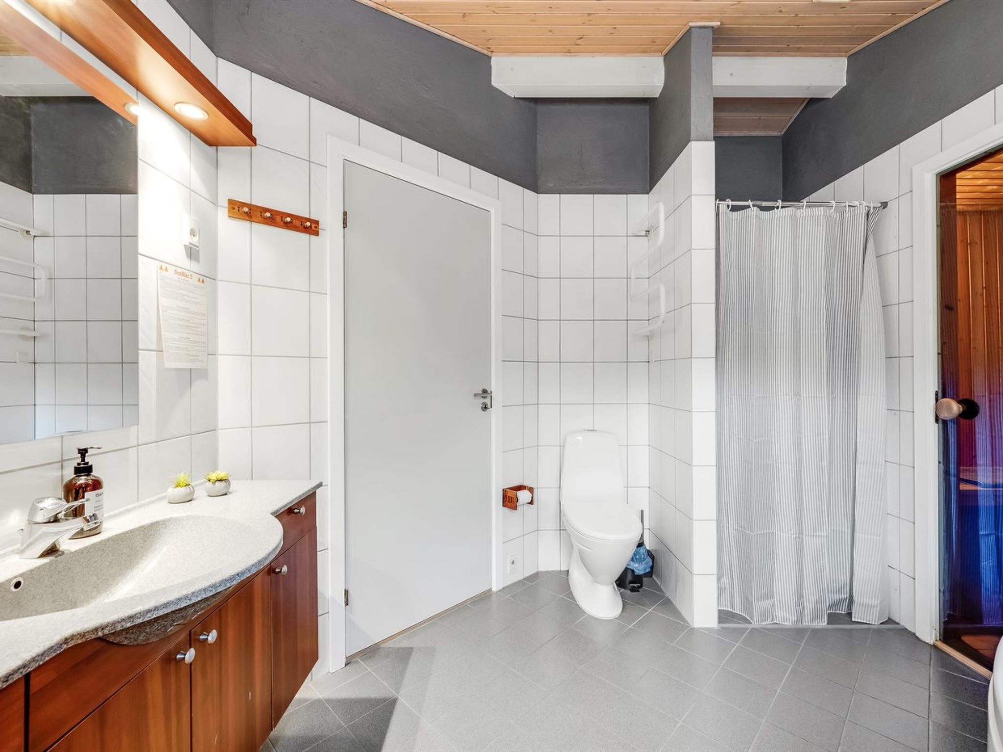 A modern bathroom with a wooden vanity, white tiles, a white toilet, and a shower curtain.