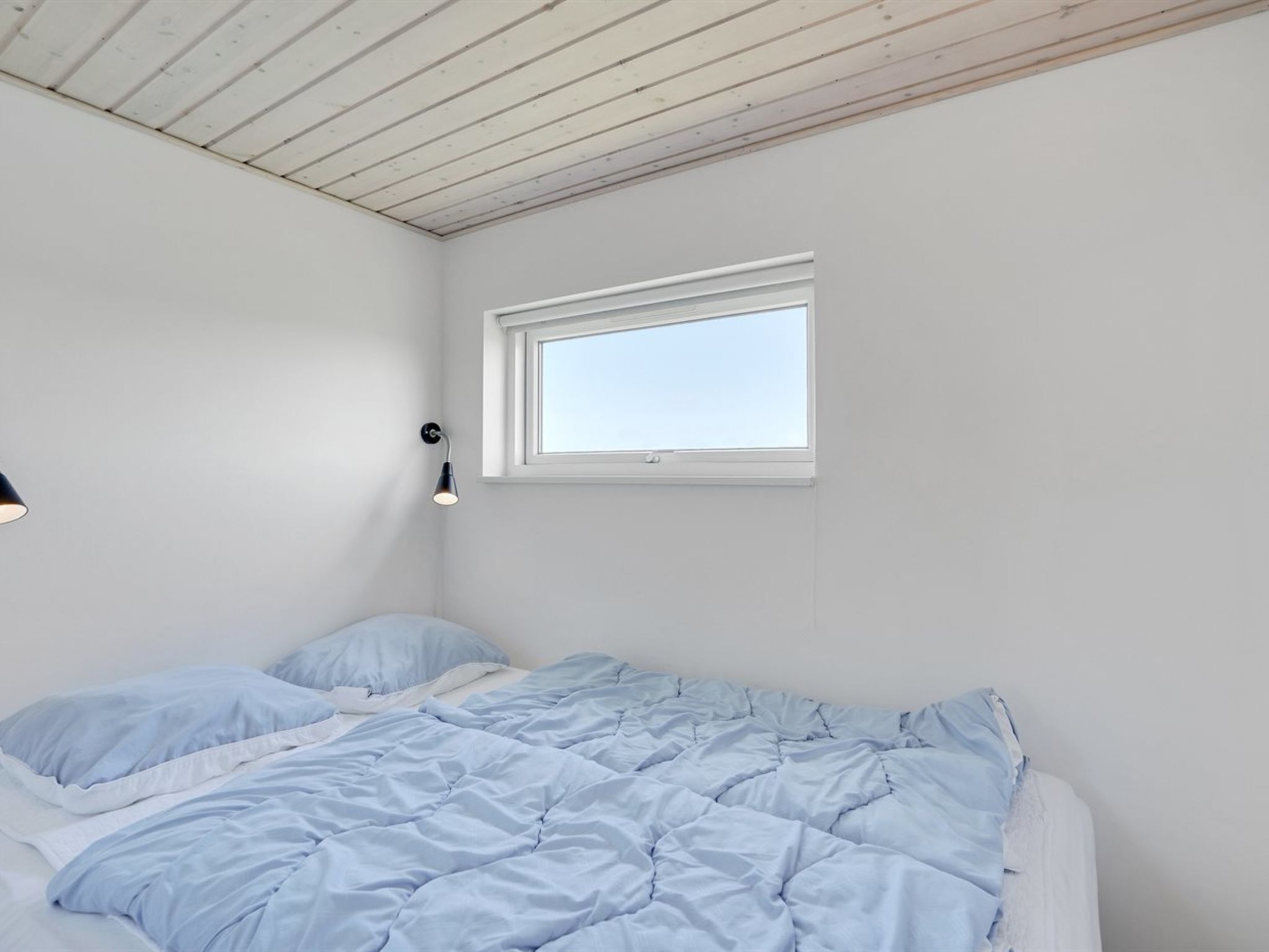 A bedroom with a bed, a window, and a wall-mounted light fixture.