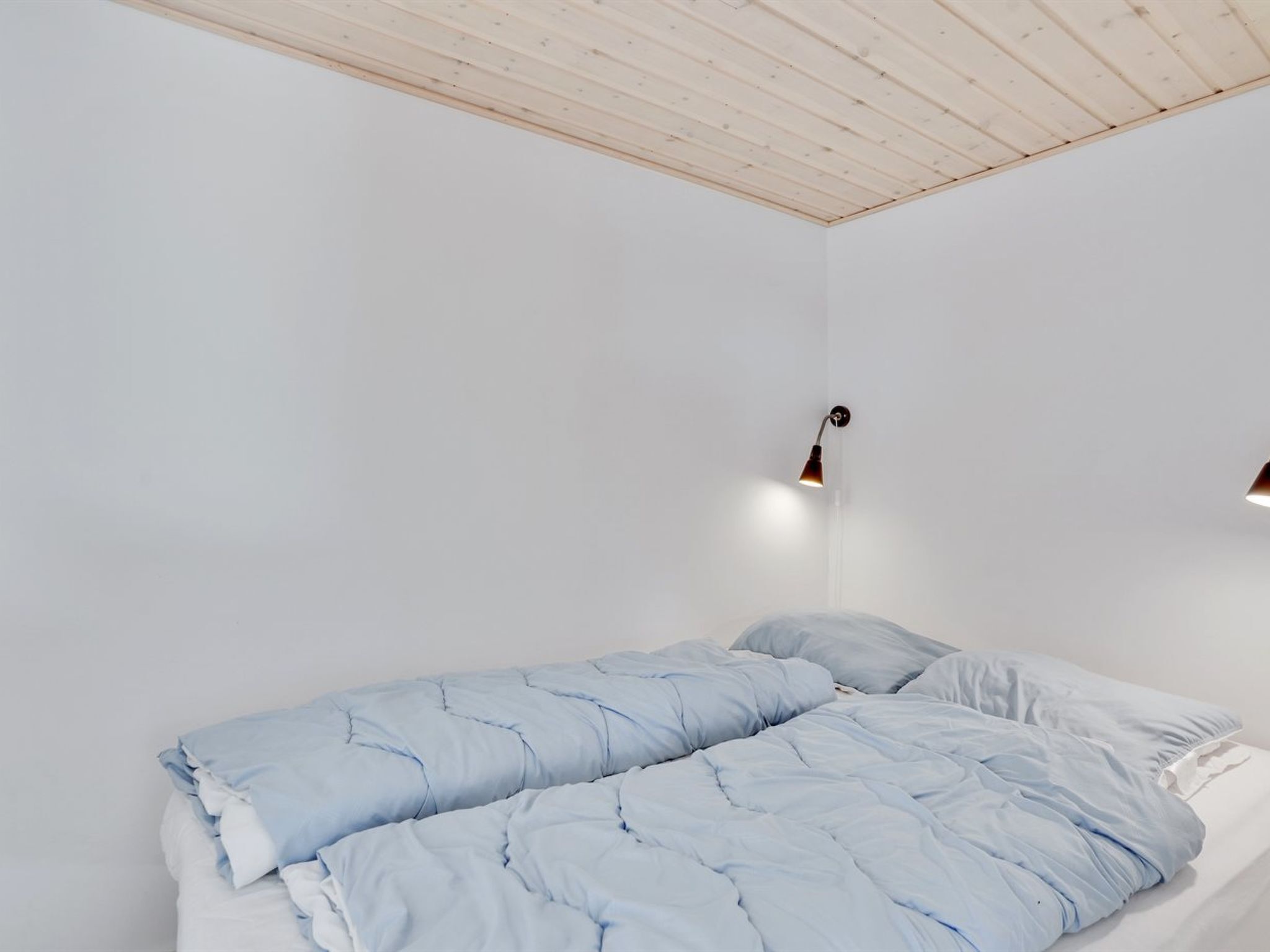 Ein schlicht eingerichtetes Schlafzimmer mit einem Einzelbett, weißen Wänden und einer Holzbalkendecke.