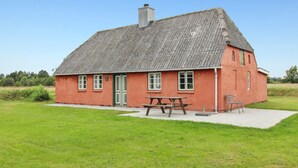 Ett hus byggt av rött tegel med ett halmtak, en grön dörr och ett picknickbord på framsidan av trädgården.
