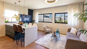 Uma sala de estar moderna com um sofá, uma mesa de centro e uma televisão. Há uma área de cozinha com uma mesa de jantar e cadeiras.