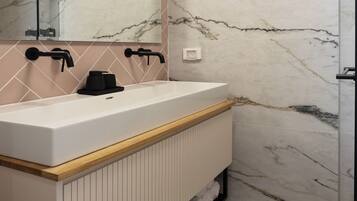 Une salle de bain avec un mur en marbre, un lavabo blanc, des robinets noirs et un meuble-lavabo en bois.