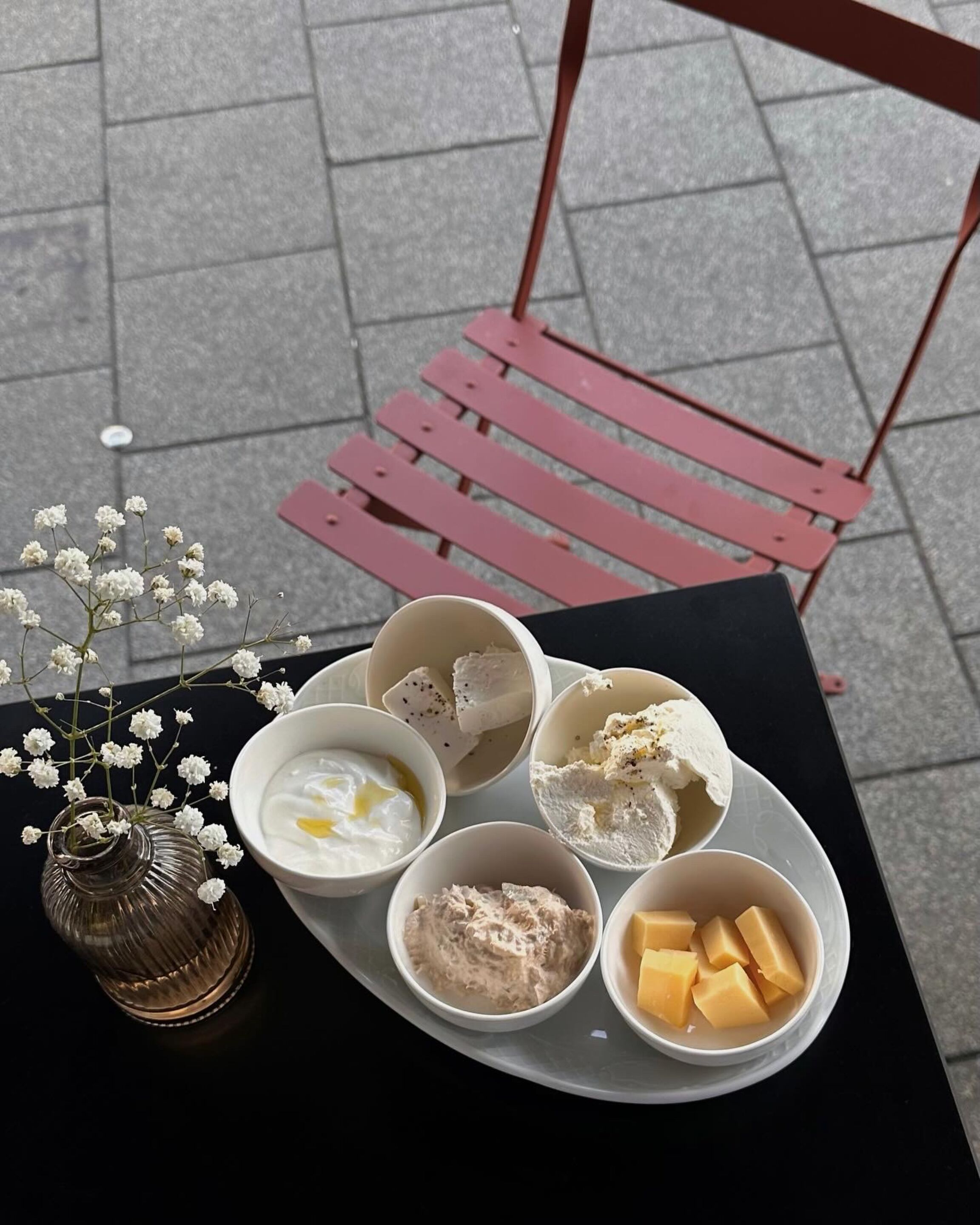 A table with a plate of food including bowls of yogurt, ice cream, and cheese, and a vase with flowers.