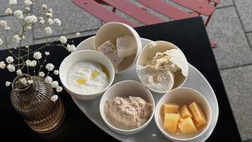 A table with a plate of food including bowls of yogurt, ice cream, and cheese, and a vase with flowers.