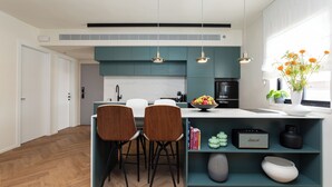 Uma cozinha moderna com armários verde-água, uma ilha central com banquetas e iluminação pendente.