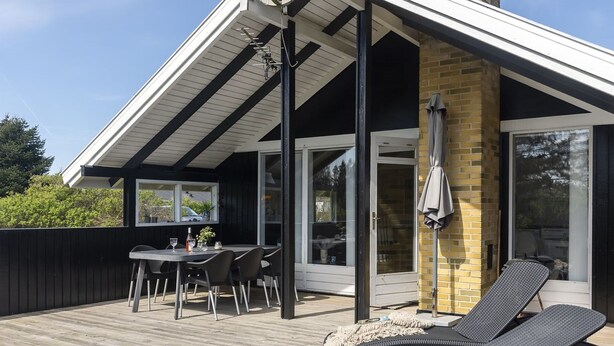 Eine Terrasse mit Tisch und Stühlen, einer Liege und einem überdachten Bereich mit Backsteinmauer und Glastüren.