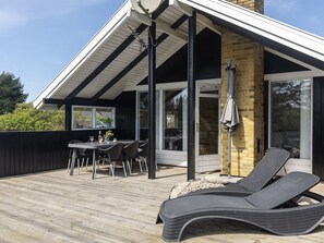 Une terrasse avec une table et des chaises, un fauteuil de relaxation et un espace patio couvert doté d’un mur en briques et de portes vitrées.