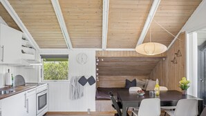 Eine moderne Küche mit weißen Schränken, einer Holzbalkendecke und einem Essbereich mit dunklem Tisch und weißen Stühlen.
