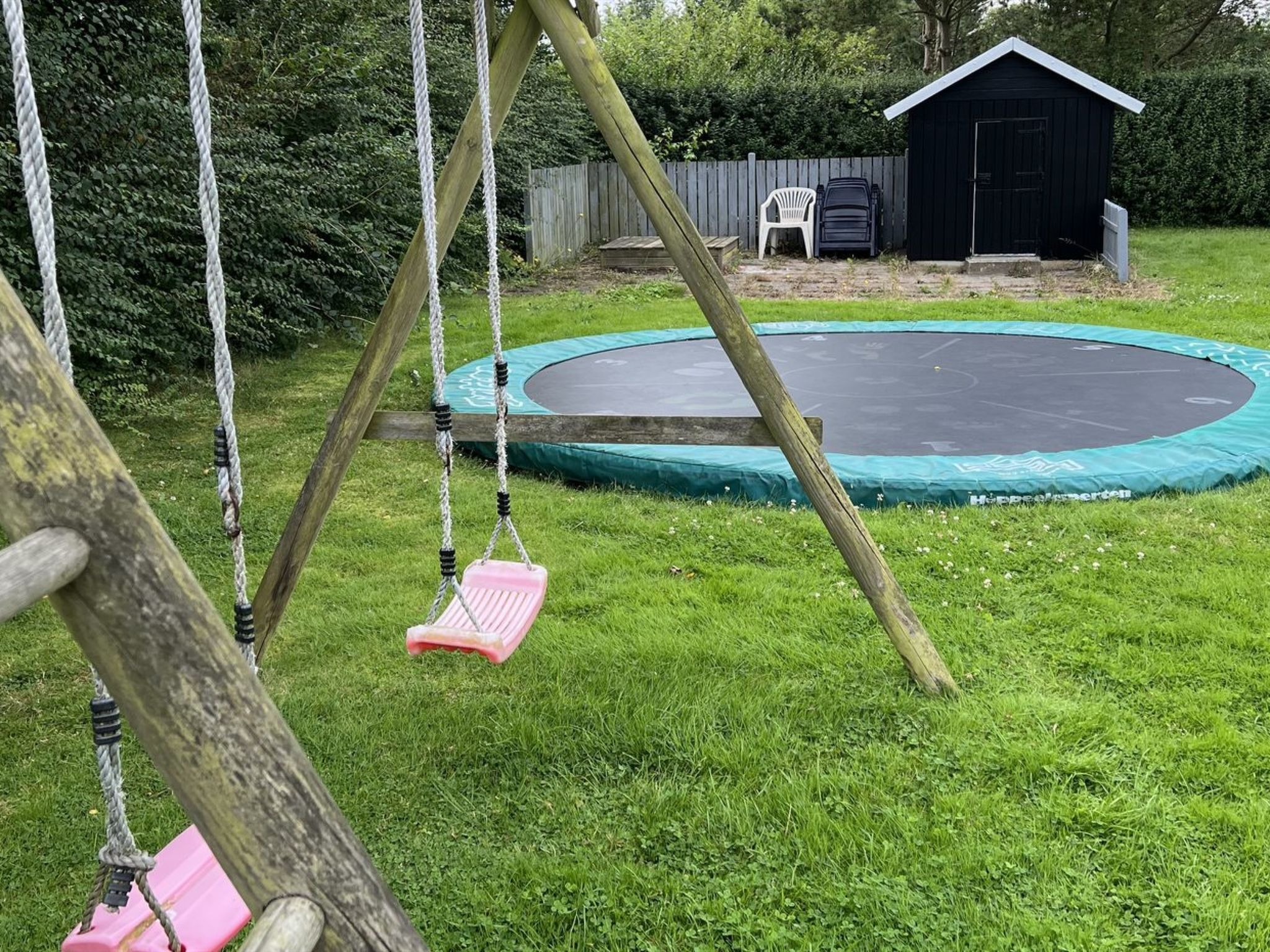 A backyard with a swing set, a trampoline, and a shed.
