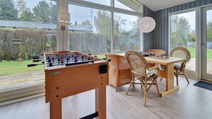 Un'ampia stanza con grandi finestre, un tavolo da calcio, un tavolo da pranzo con sedie e vista sull'esterno.