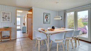 Un'area pranzo moderna con un tavolo e sedie bianche, una lampada a sospensione e vista sull'esterno.