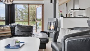 Ein modernes Wohnzimmer mit Kamin, Ledersofas, einem Esstisch mit Tablett und Blick durch große Fenster.