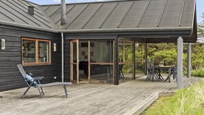 Ein modernes Haus mit einer Holterrasse, einer überdachten Veranda und einem Schornstein.