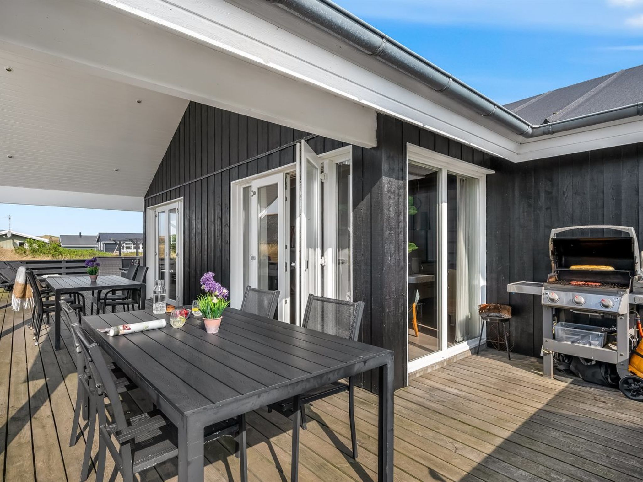 A covered outdoor area with a dining table, chairs, a grill, and a sliding glass door leading to a covered patio.