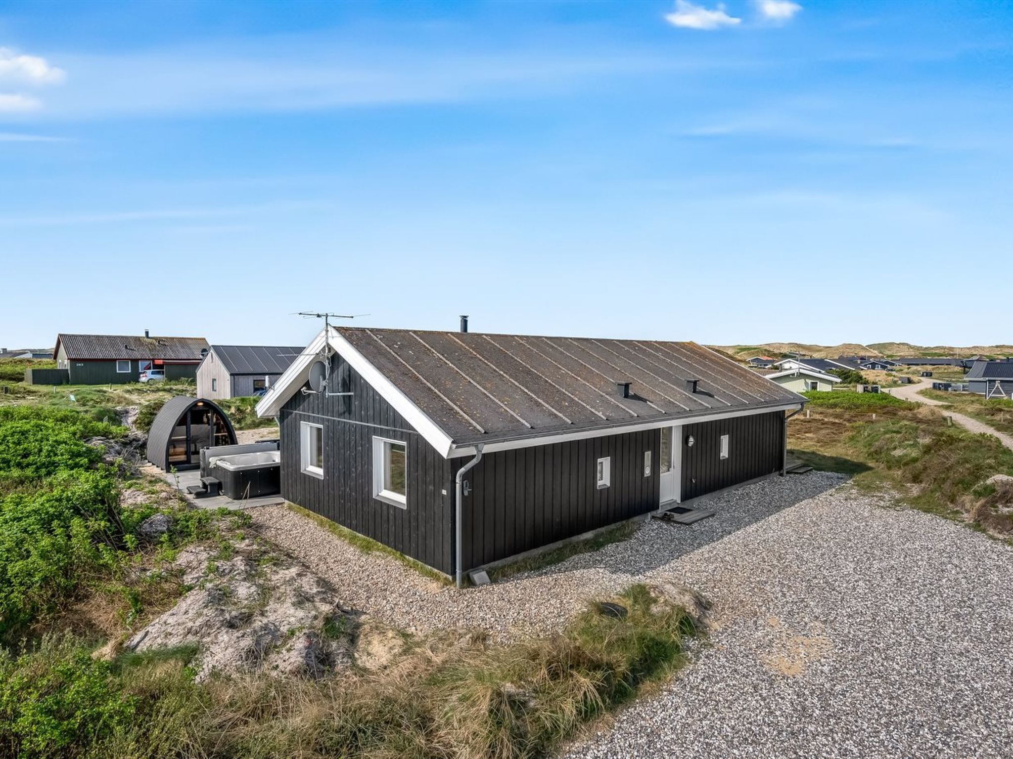 Un bâtiment moderne, de plain-pied, doté d’un toit en pente, d’une petite dépendance attenante et d’une allée gravillonnée.