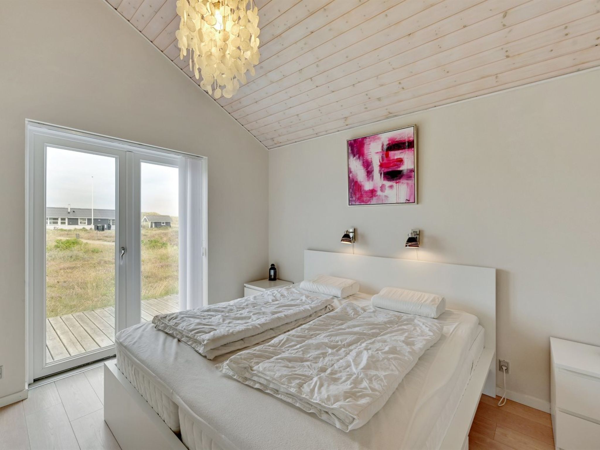 A modern bedroom with a large bed, a sliding glass door leading to a balcony, and a ceiling light fixture.