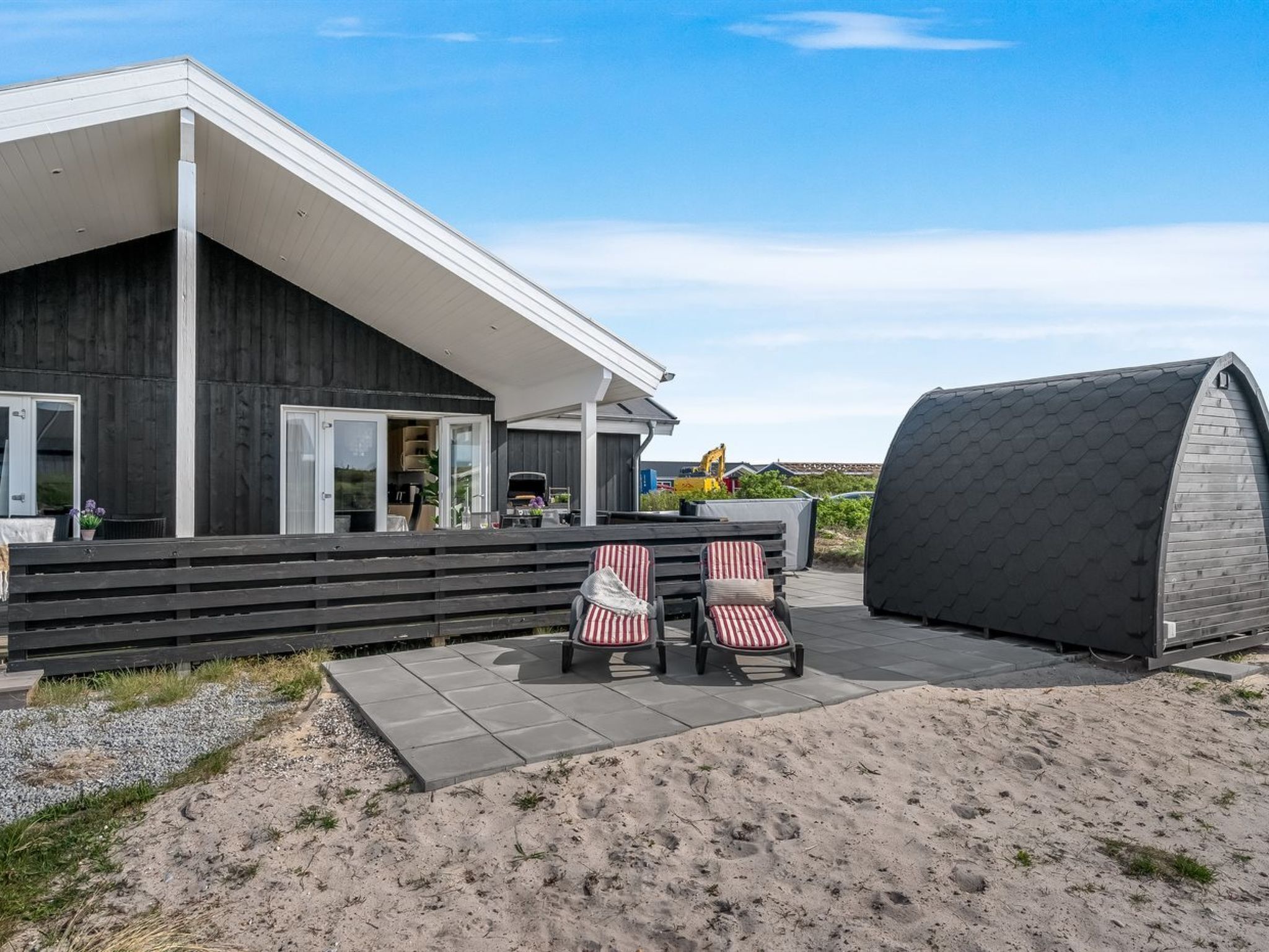 Une maison moderne dotée d’un patio couvert, de deux chaises à rayures et d’un grand abri de jardin.