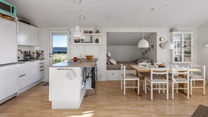 Cocina moderna con armarios blancos, una isla de madera y un comedor con sillas blancas y una mesa de madera.