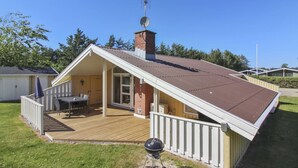 Ein Bungalow mit überdachter Terrasse, Schornstein und Satellitenschüssel.