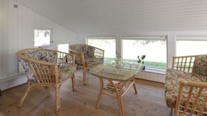 Ein Zimmer mit einem Glastisch, umringt von Korbstühlen, großen Fenstern und Blick ins Grüne.