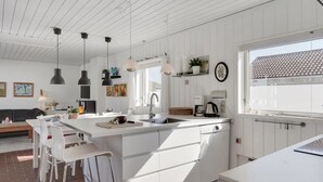 A modern kitchen with white cabinetry, a large island, pendant lighting, and a view of the outside through a window. - "Marjon" - 400m from the sea by Interhome (Pandrup)